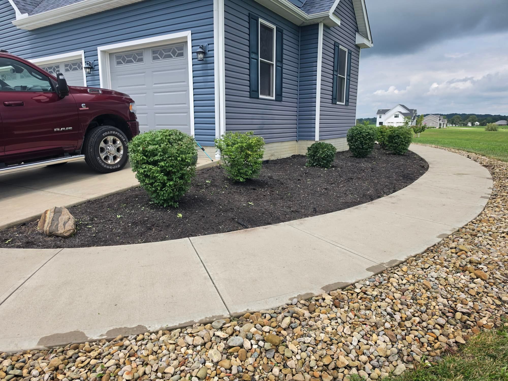 Curved walkway with fresh mulch bed, shaped shrubs, decorative boulder and river rock drainage border